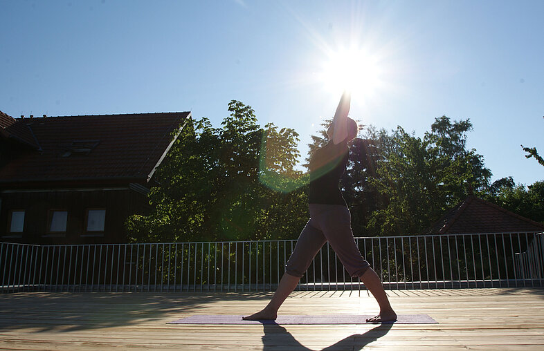 Yoga-Pose des Kriegers auf einer sonnenbeschienenen Holzterrasse im Rosenberg Ayurveda Zentrum